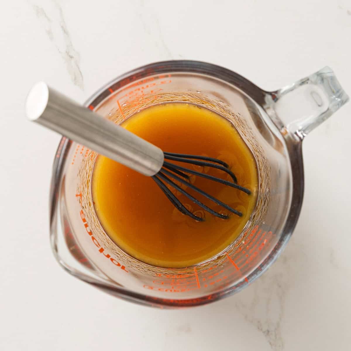 Overhead view of a vinaigrette dressing in a glass measuring cup with a whisk.